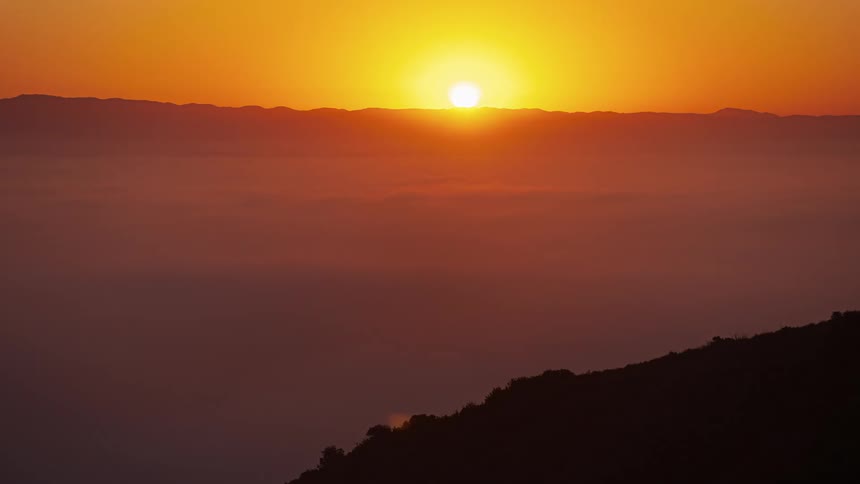 Sun rising over moving clouds next to a shadow of land