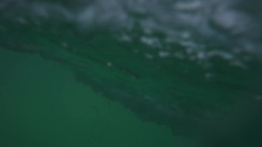 Sun shines through crashing wave and underwater under clear blue sky