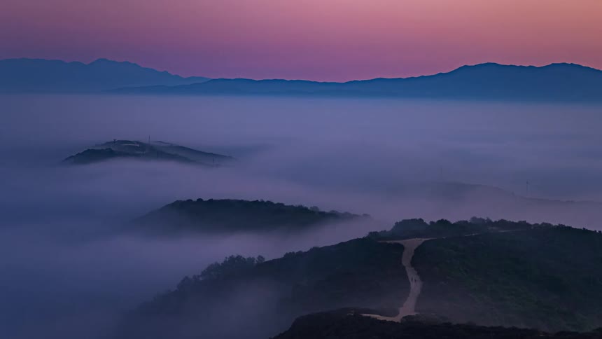 People run on a dirt trail on the top of a hill in heavy fog at sunset