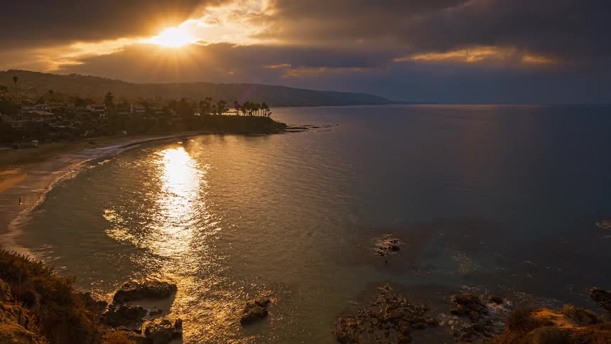 The sun is rising over a coastal area that is lined with numerous houses