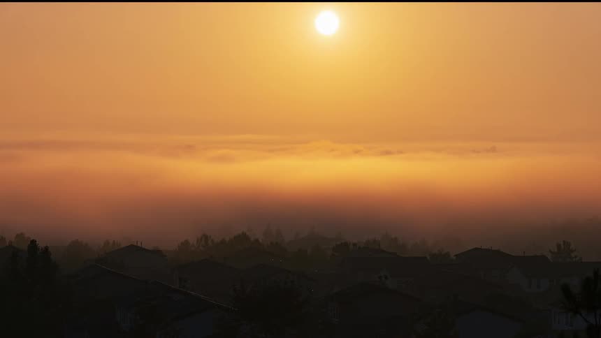 The silhouette of a neighborhood is seen beneath clouds and a rising sun