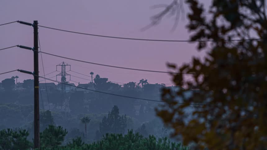 The sun sets behind the hill with houses on the horizon