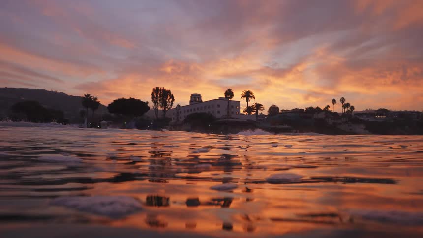 Building sits near water reflecting red sky and dotted with bobbing bits of ice