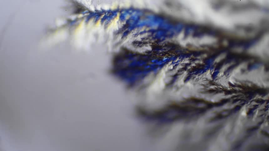 A chemical reaction shows blue and silver crystals forming under a microscope