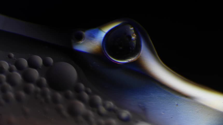 A chemical reaction shows a silver liquid with bubbles and a white light shimmer passing over it