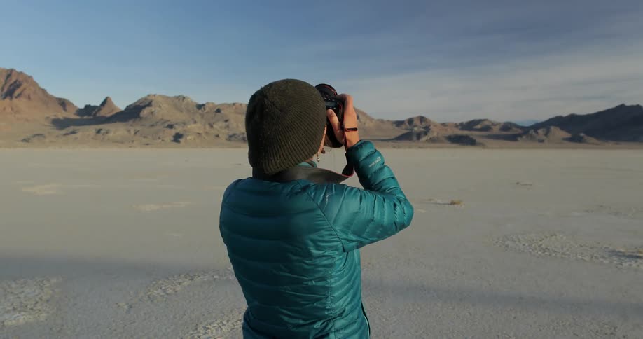 A woman stands in a desert landscape taking pictures of something above her