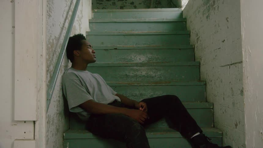 Man with a grey shirt black pants and boots sits on turquoise stairs