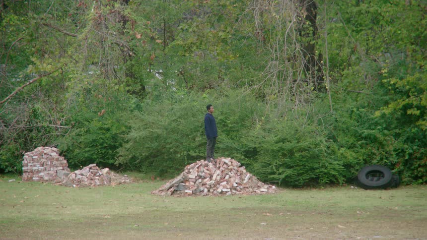 A young male stands atop a pile of bricks while looking off into the distance