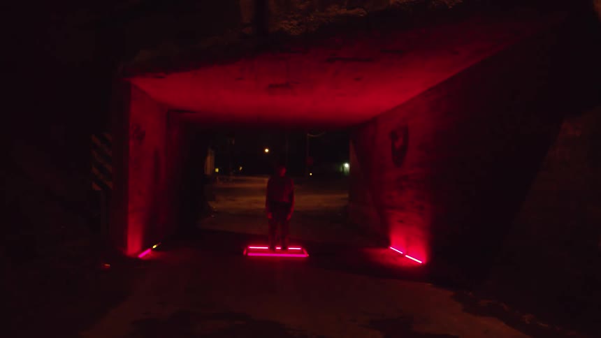 Male figure standing in the center of a red flashing light in a dark tunnel like structure