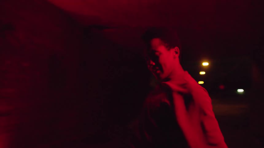 A teenager waves his hands around while dancing in a tunnel at night