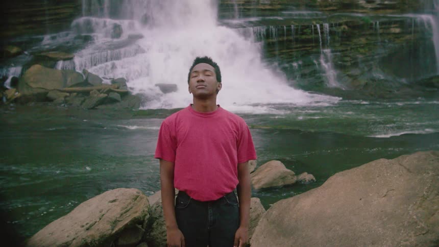 A black male standing near a waterfall meditating