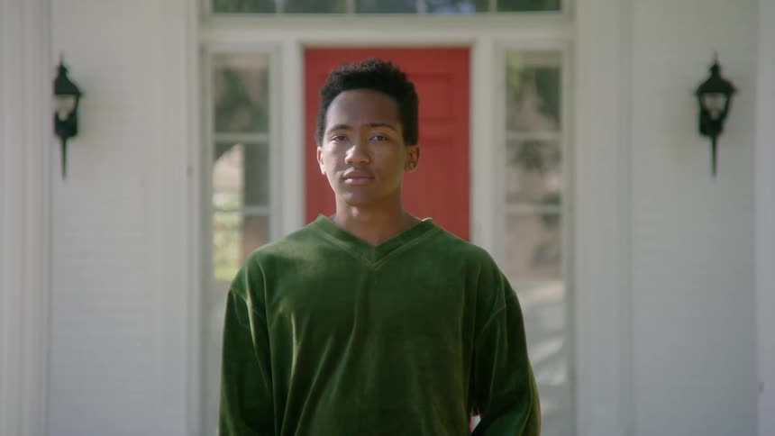 Teenage boy standing outside at daytime in front of a house with a red door