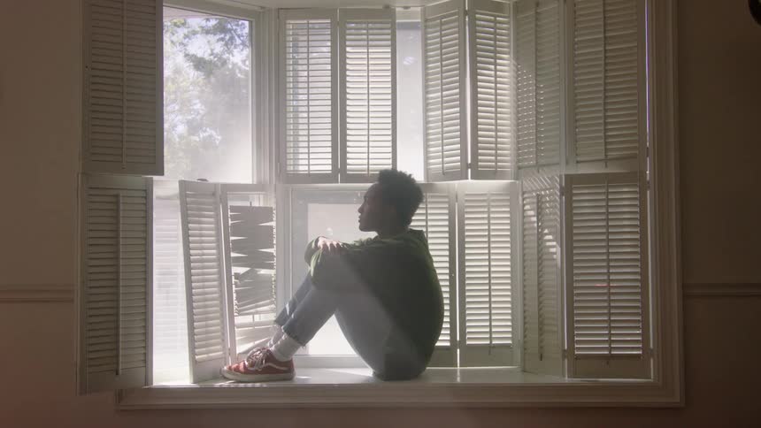 Man with a sweater pants and red shoes sits on windowsill