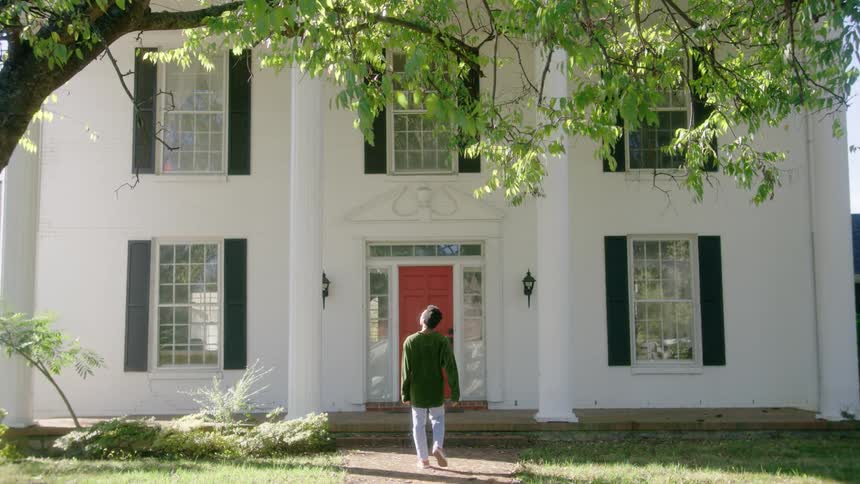 A person walks towards the front red door on a white house