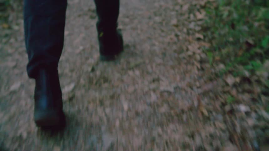 Man with a red shirt and black pants walks along a dirt road in the woods