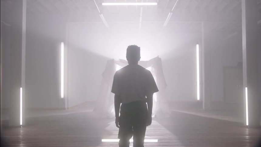 A man walks through the lobby of a building with several columns of light and toward a display in the center with a curtain surrounding a large light source