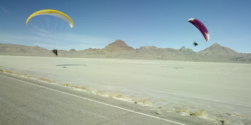 Two motorized hang gliders fly above a desert landscape