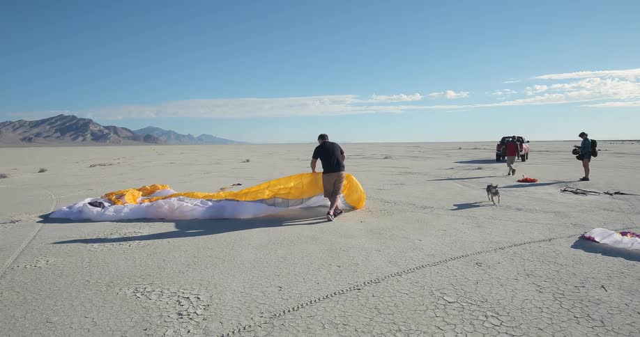 People unrolling their parachutes on an open plain