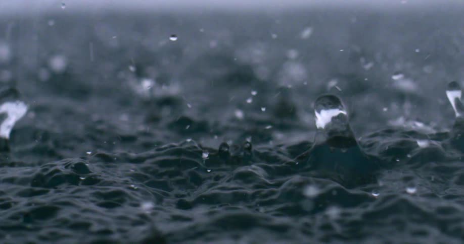 Rain water droplets pouring down into a body of water