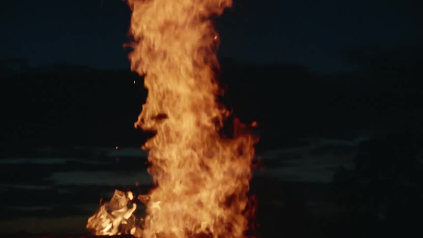 Orange flames and embers rise against a night sky