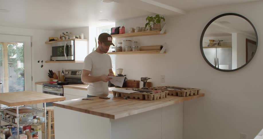 A man stands at his kitchen counter and unfolds a booklet to read