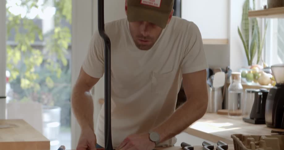 A man stands in a kitchen assembling something on a counter during the day