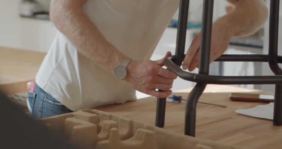 A man stands and tightens a screw into a leg of stool