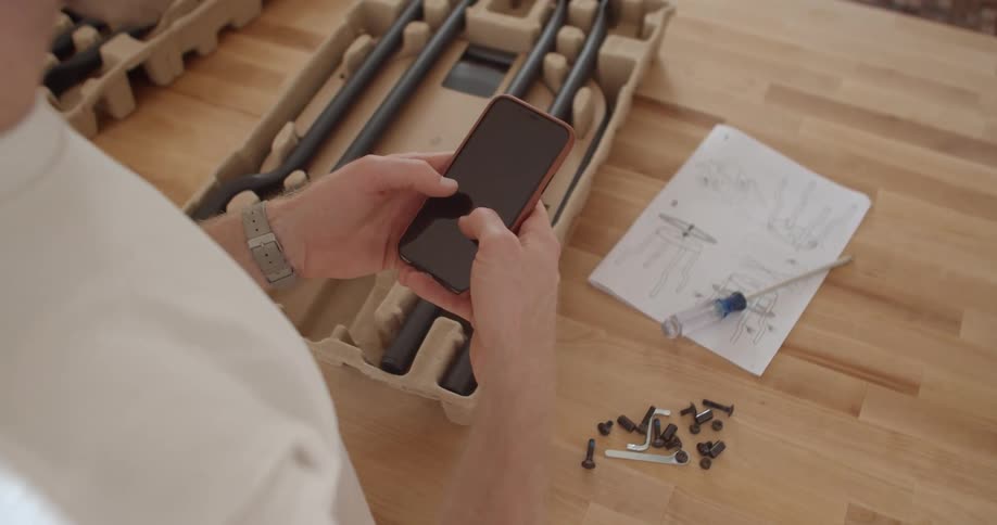 A man looks at smart phone while in the middle of assembling a coffee table