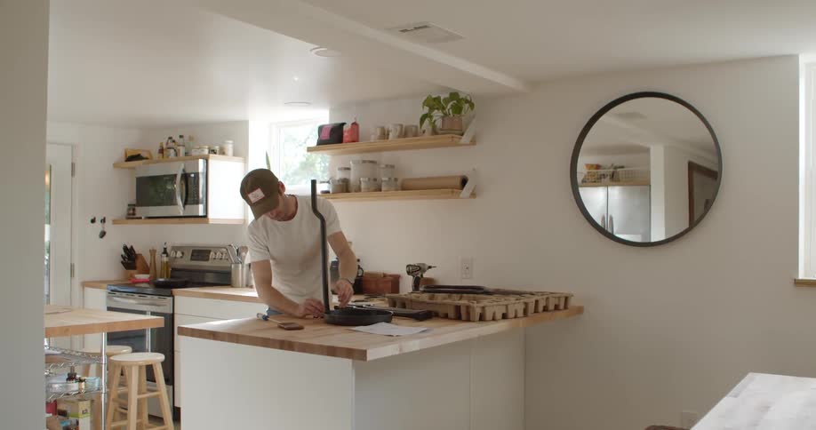Man standing in his kitchen at daytime with an unassembled piece of black furniture on top of the counter fixing it