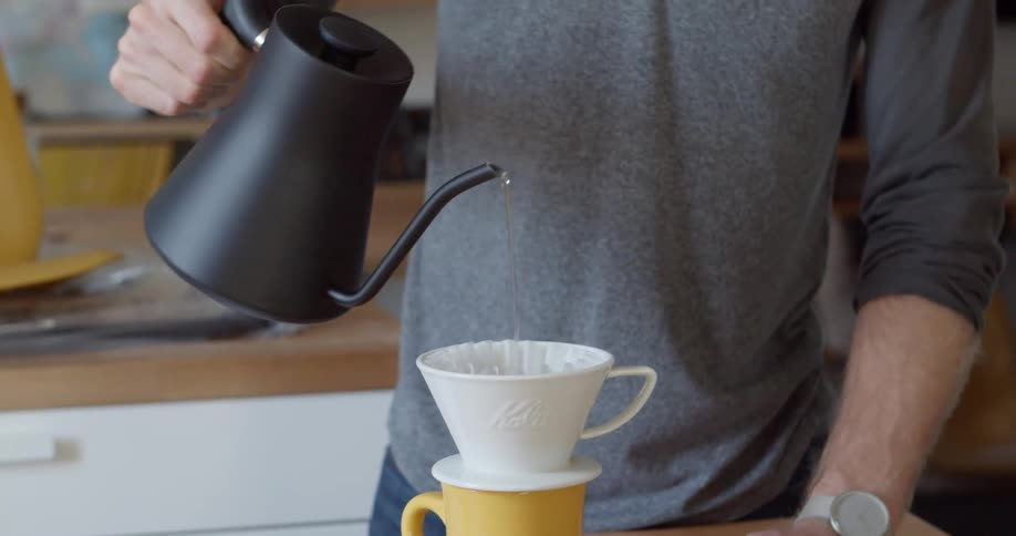 A man pours water out of a kettle into a pour over coffee maker