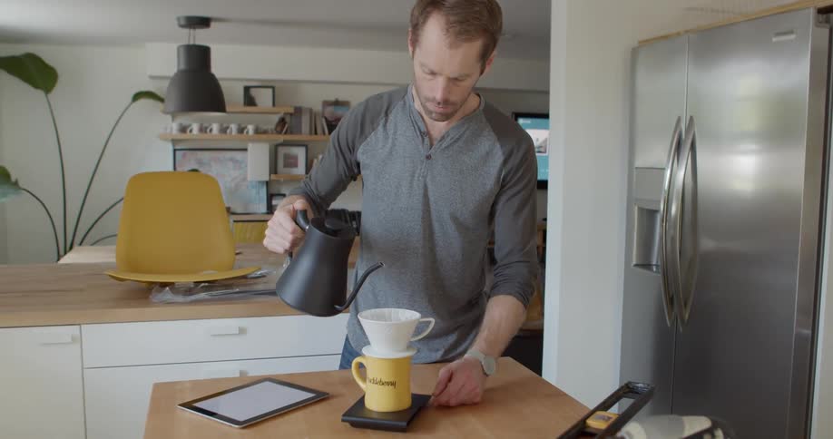 A man holds a kettle in his kitchen to make coffee