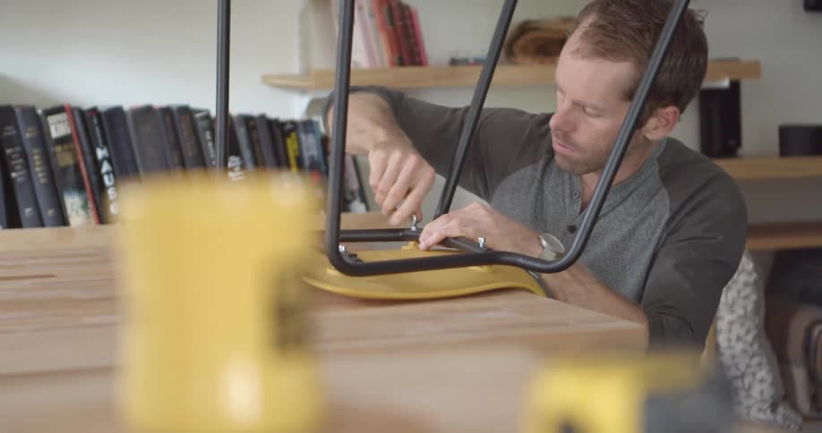 A man tightens a screw on the bottom of a dining room chair