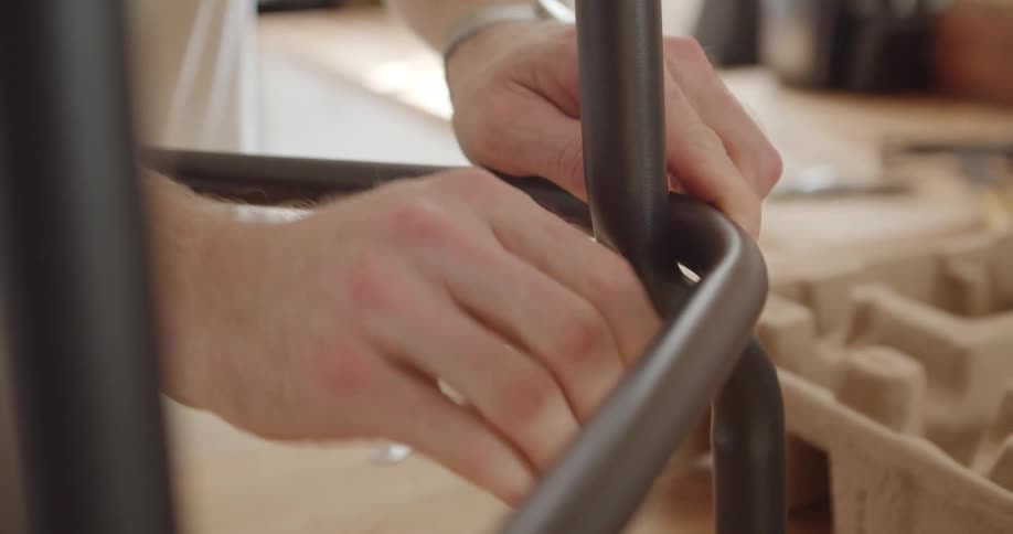 Hands tightening a screw into a piece of metal indoors