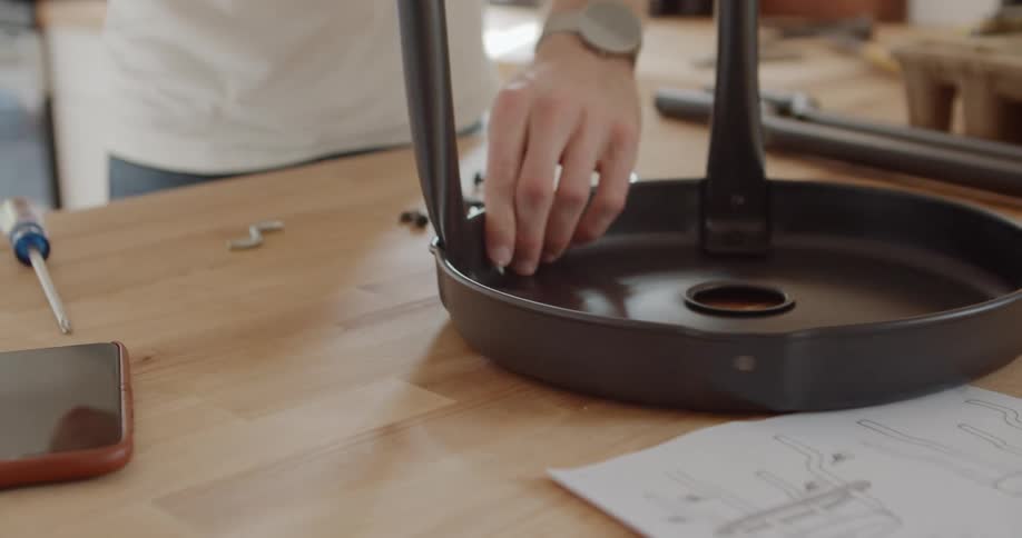 Man follows instruction sheet while putting together metal furniture on wooden table