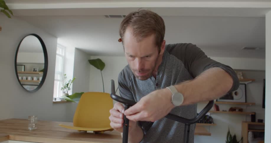 A man stands and puts a bolt to assemble a piece of furniture indoors