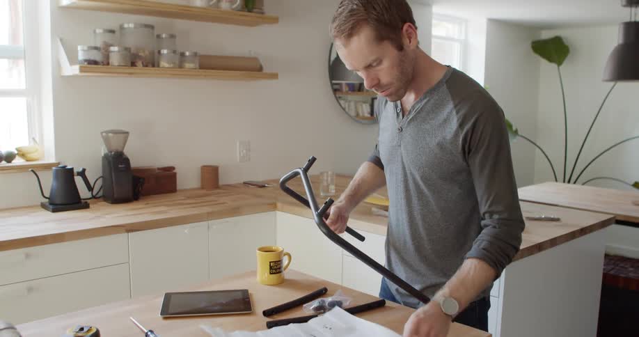 A man stands in his kitchen looking at a metal rod and paper instructions
