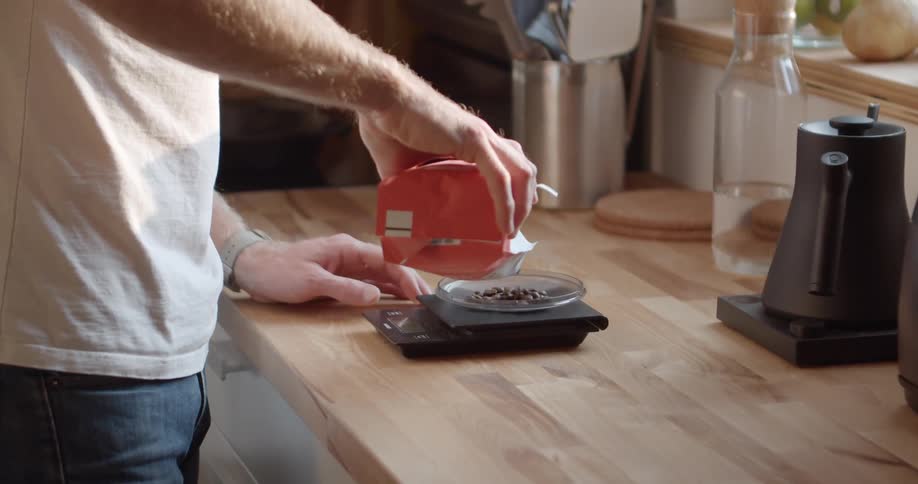 Male pouring coffee beans from bag onto a small weighing scale