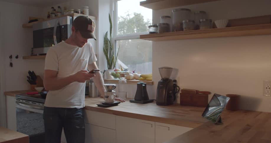 A man stands looking at his smartphone while waiting for his coffee to finish