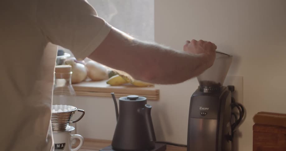 A man puts coffee beans into a grinder on his kitchen counter