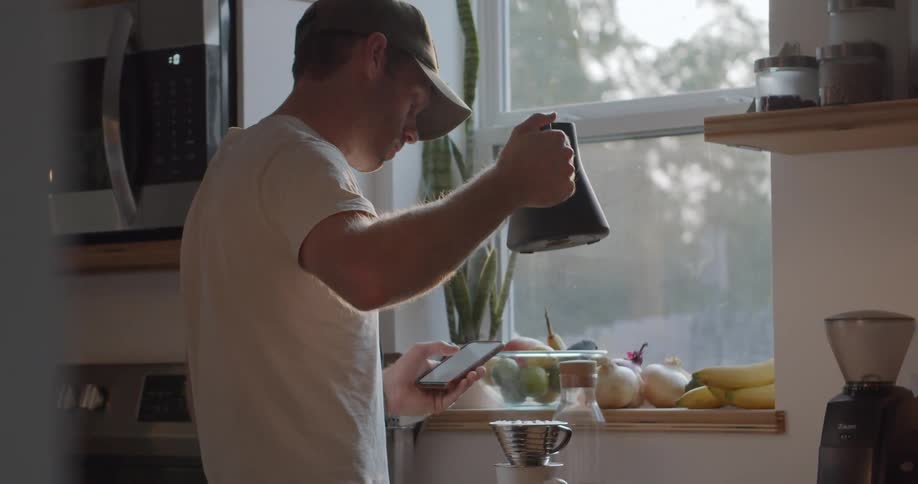 A young man in a hat carefully pours hot water into a pour over coffee maker
