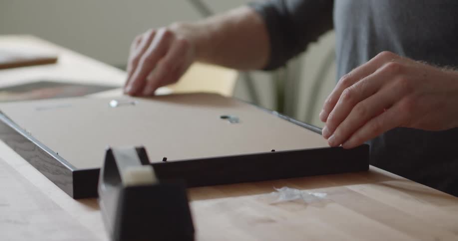 A man carefully places the backing cover onto a picture frame