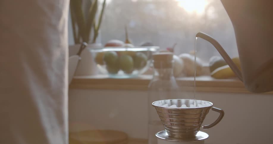 Silver water kettle pouring hot water in a coffee filter at day time inside of a kitchen in a house