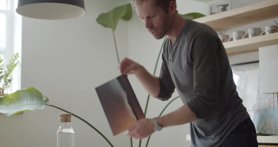 Man in his home putting pictures into a picture at a dining room table