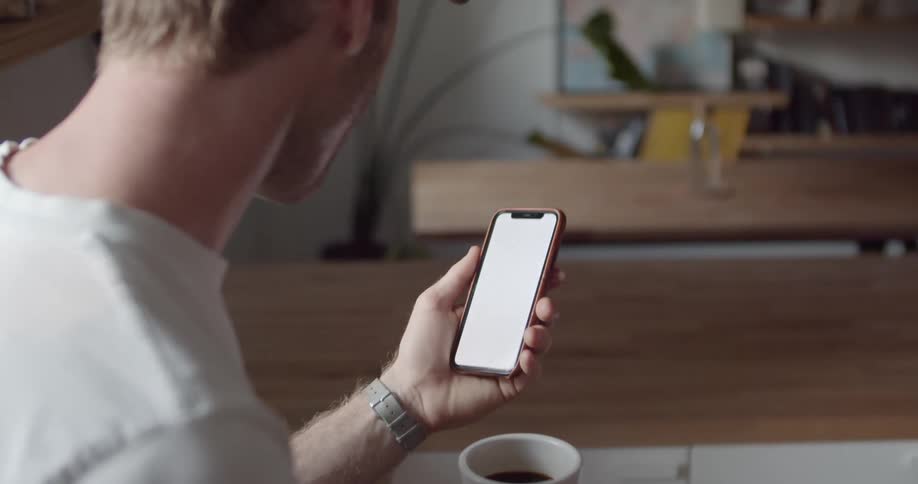 A man holds up his coffee mug to toast someone during a video call on his smartphone