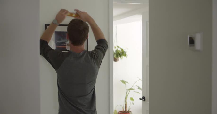 A male using a wall level to mount a picture in a hallway