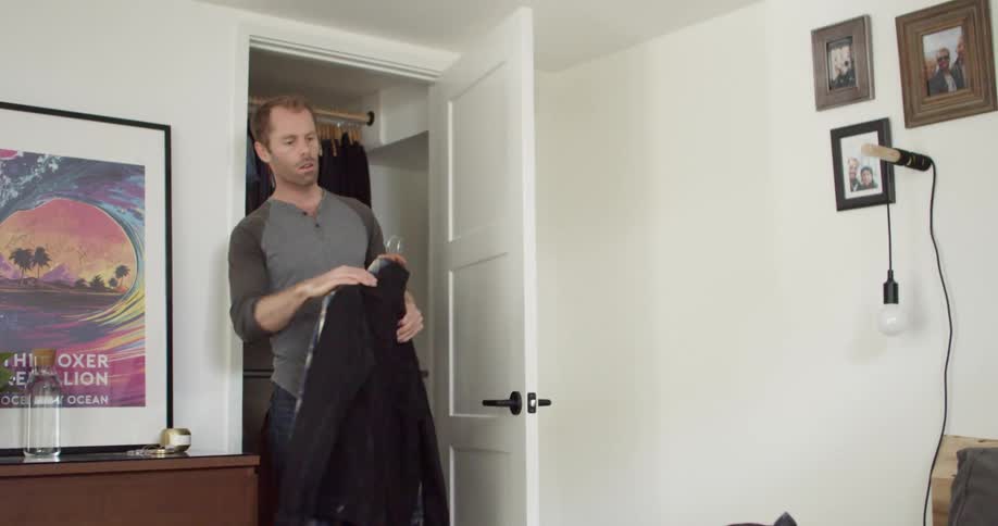 Man taking clothes out of his closet at day time and putting them into a suitcase on a bed