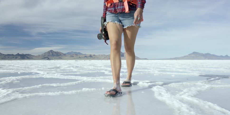A photographer wearing shorts and sandals as she walks over snow