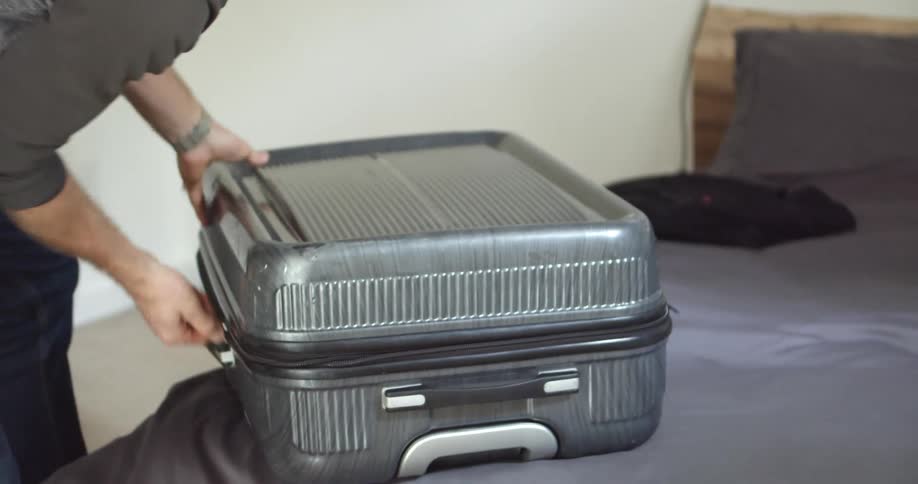 A man zips up a suitcase on his bed