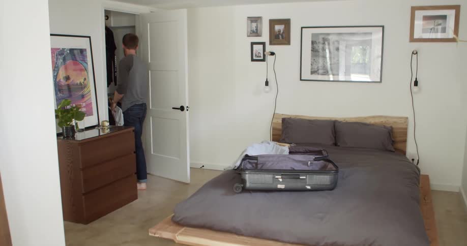 A man takes shirts from his closet and puts them on a suitcase