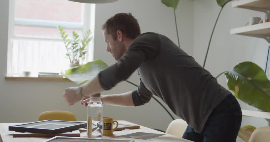 A man at home sits at his table and looks at pictures in frames